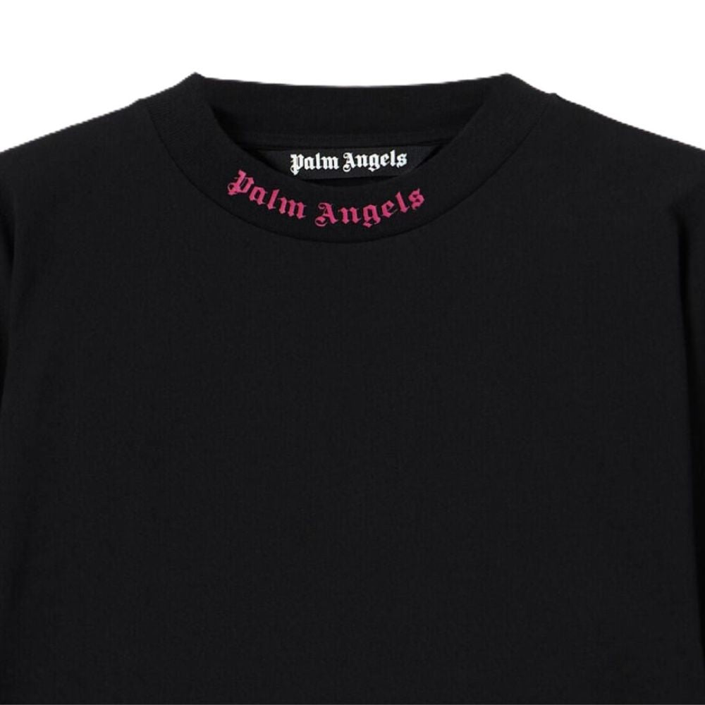 Close-up of a black crewneck sweatshirt featuring the Palm Angels brand name printed in white Gothic font inside the collar and in pink Gothic font across the front of the collar.