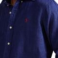 Close-up of a navy blue long-sleeve button-up shirt with a red embroidered Polo pony logo on the chest, worn by a model.
