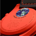 Close-up of the back of a bright orange-red Swatch watch showing the Earth graphic and embossed text including 'MISSION ON EARTH' and 'SWATCH SWISS MADE WATER RESISTANT'.