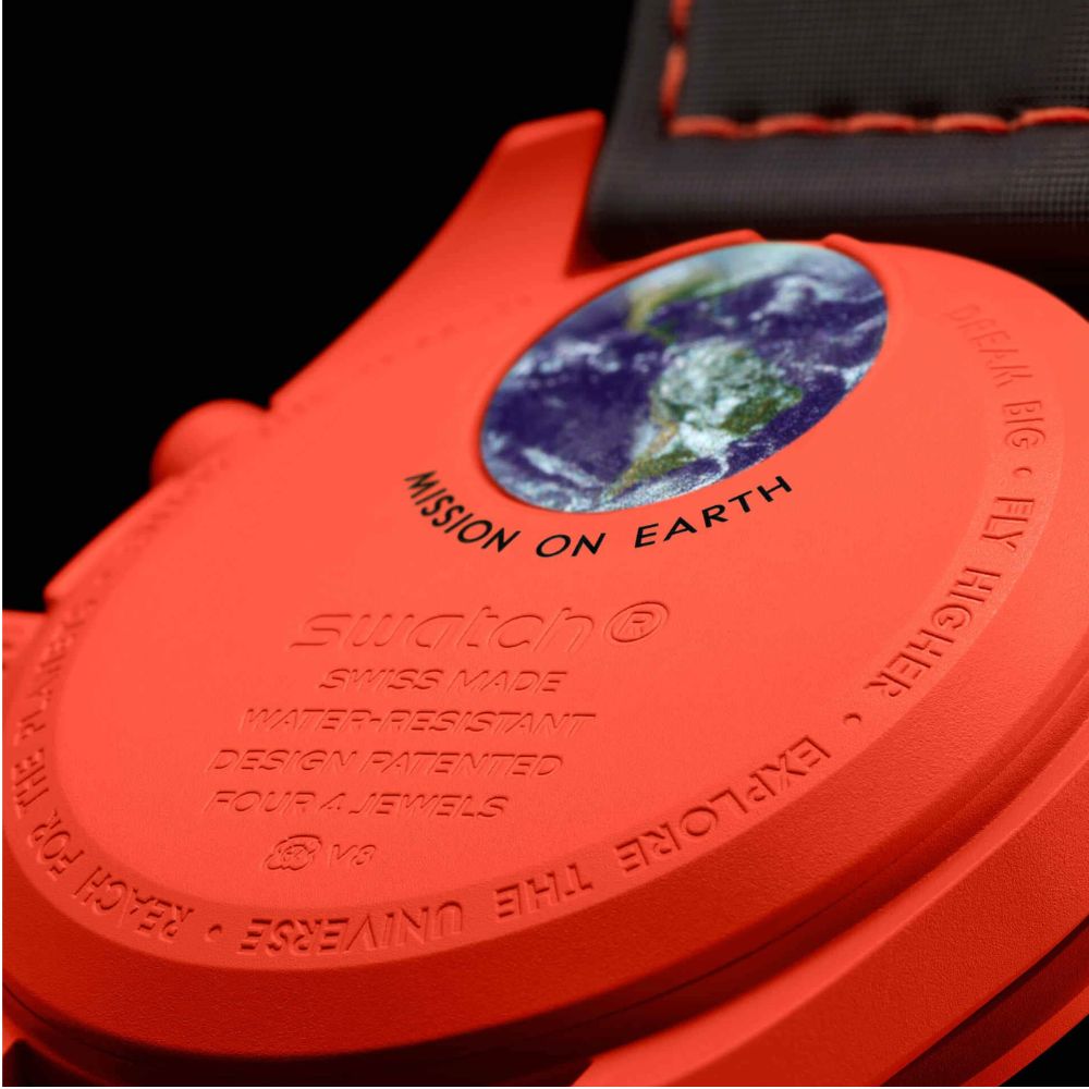 Close-up of the back of a bright orange-red Swatch watch showing the Earth graphic and embossed text including 'MISSION ON EARTH' and 'SWATCH SWISS MADE WATER RESISTANT'.