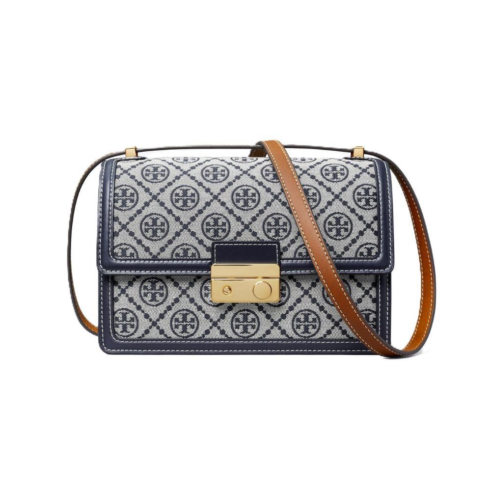A Tory Burch handbag with a navy and white patterned canvas body, a brown leather shoulder strap, and a gold-tone turn-lock clasp, shown on a plain white background.
