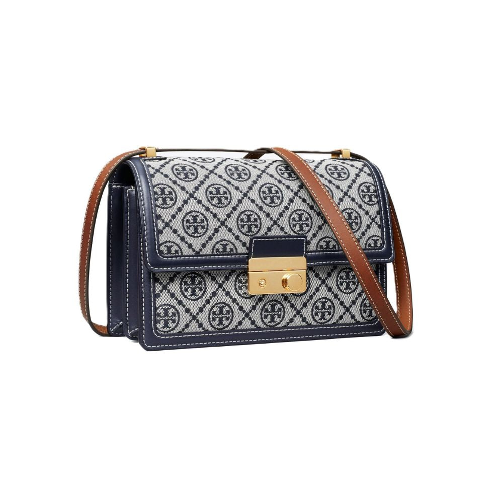 A Tory Burch crossbody bag featuring navy blue and white monogram canvas, navy blue leather trim, a gold-tone turn-lock clasp, and a brown leather shoulder strap, shown against a plain white background.