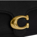 Close-up of a black textured leather handbag featuring a large polished gold-tone C-shaped metal clasp.
