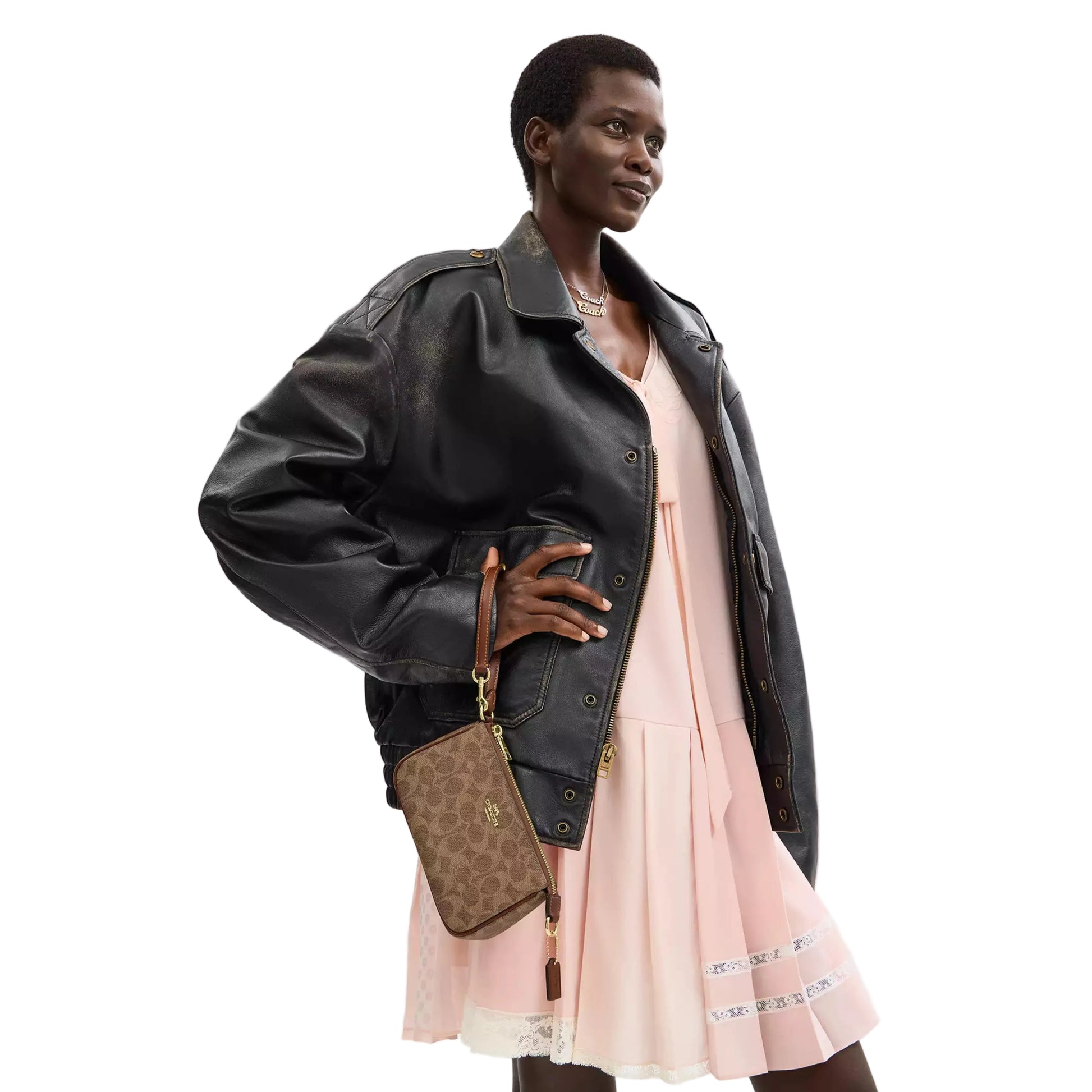 Woman wearing a black leather jacket and pink dress holding a Coach bag on a white background